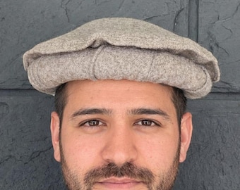May include: A light gray Pakol hat, a traditional wool cap with a rounded crown and a rolled brim. The hat is made of a soft, textured material and is worn on the head. The hat is a neutral color and can be worn by anyone.
