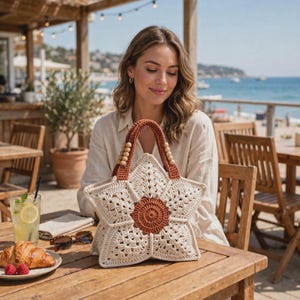Könnte beinhalten: Eine sternförmige Häkeltasche mit einem cremeweißen Granny-Square-Muster und einem einfarbigen, rostfarbenen kreisförmigen Mittelteil. Die Tasche hat zwei robuste, rostfarbene Häkelgriffe, die an jeder Seite mit kleinen hellen Holzperlen verziert sind.