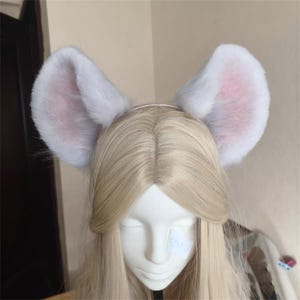 Puede incluir: Orejas de ratón blancas y esponjosas con detalles rosas en el interior, sujetas a una fina diadema rosa. Las orejas son grandes y redondeadas, creando un aspecto juguetón y caprichoso. Perfecto para cosplay o fiestas de disfraces.