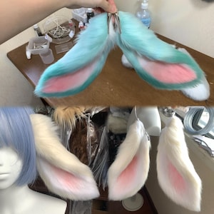 Puede incluir: Un par de orejas de animal de piel sintética con un degradado de azul claro y blanco con detalles interiores en rosa suave, unidas a una pinza de metal. Debajo, un conjunto de orejas de piel sintética blanca con centros rosas en un maniquí.