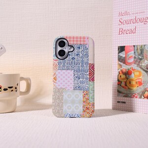 May include: A rectangular smartphone case featuring a patchwork design of various patterns including blue floral motifs, pink geometric shapes, orange polka dots, and a red checkered top section, with a dual-lens camera cutout at the top left.