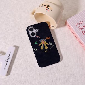 May include: Black phone case featuring a cartoon character in a yellow coat. The case has a camera cutout and a design with a dragonfly, a green triangle, a moon, and a cookie. A white object with the text "Neat & uniform" is in the image.