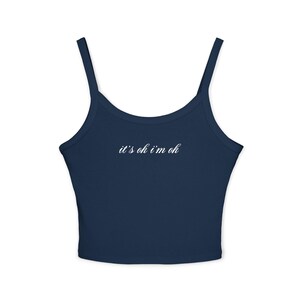 May include: A navy blue crop top with thin straps. The white cursive text, "it's ok i'm ok" is printed across the chest. The top is a solid colour and appears to be made of a soft material.