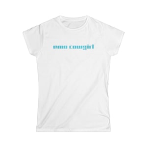 May include: White t-shirt featuring the text "emo cowgirl" in light blue. The text is centrally placed. The shirt has a crew neck and short sleeves. The fabric appears to be a soft, lightweight material.