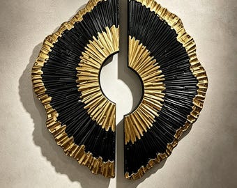 May include: A two-piece wall sculpture featuring a circular design with a black centre and gold-toned edges. The surface is textured with radiating lines that extend from the inner opening to the irregular, scalloped outer perimeter.