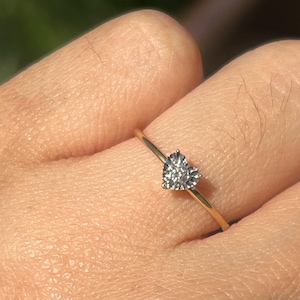 Peut inclure: Une bague en or délicate ornée d'un diamant en forme de cœur. Le corps de la bague est fin et doré, et le diamant scintille d'une teinte gris clair. La bague est un bijou simple mais élégant.