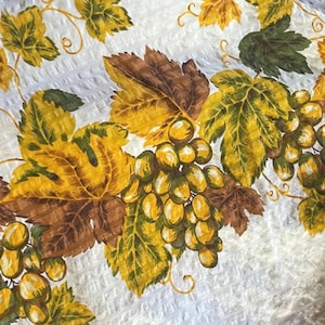 May include: White tablecloth with a repeating pattern of embossed texture and scattered leaves. The border features a brown stripe with a yellow accent. A large grape cluster design with yellow, green, and brown leaves and grapes is featured.