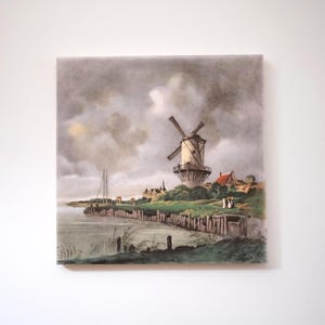 May include: A square canvas print of a vintage landscape scene. The artwork shows a windmill on a grassy hill near water, under a cloudy sky. The colour palette includes muted greens, browns, and greys.