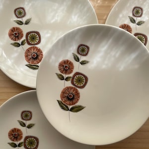 May include: Four off-white ceramic plates with a floral design. The design features orange, brown, and green flowers with dark green leaves. The plates are round and have a simple, elegant design.