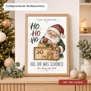 May include: A framed print featuring a Santa Claus illustration holding a brown paper bag with a 50 Euro banknote displayed in a rectangular cutout. The text reads: FROHE WEIHNACHTEN, HO HO HO, HOL DIR WAS SCHÖNES!, and Von Herzen für dich.