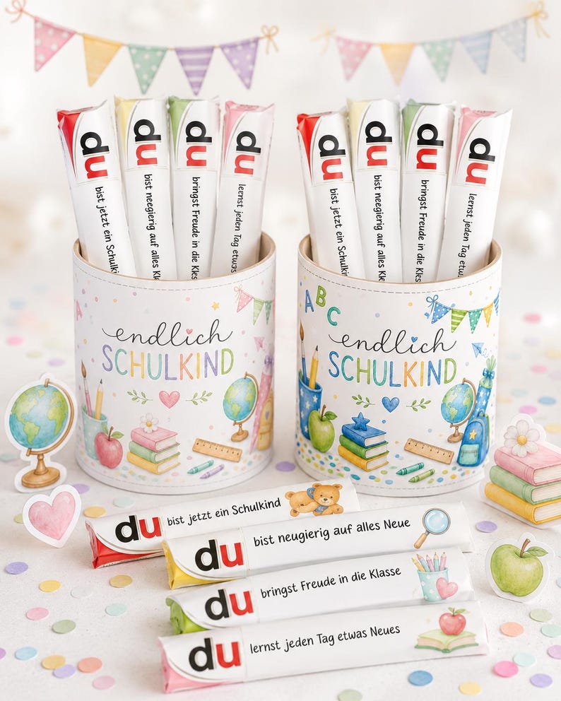 May include: Two cylindrical containers decorated with school-themed illustrations and the text "endlich SCHULKIND". Each holds four white candy bars labeled "du" followed by German phrases. Four additional candy bars lie horizontally in front.