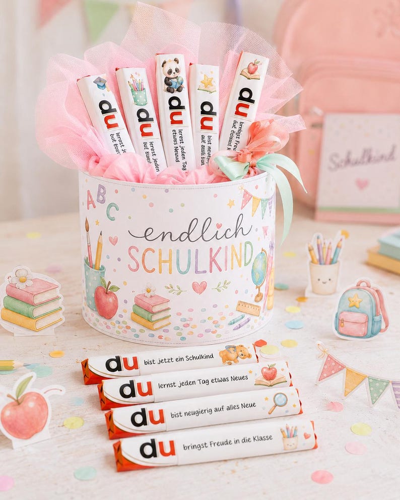 May include: A cylindrical gift box decorated with school-themed illustrations and the text "endlich SCHULKIND," filled with pink tulle and five chocolate bars labeled "du" with various phrases and icons, plus four additional chocolate bars in front.