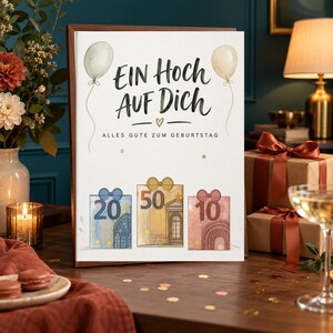 May include: A white birthday greeting card with the text "EIN HOCH AUF DICH" and "ALLES GUTE ZUM GEBURTSTAG" in black script and print. The card features two balloons and three rectangular illustrations resembling euro banknotes of 20, 50, and 10.