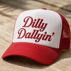 May include: A red and white trucker hat featuring a red mesh back and a solid red brim. The white front panel displays the embroidered red text Dilly Dallyin' in a cursive script font. The cap includes a red button on the top center.