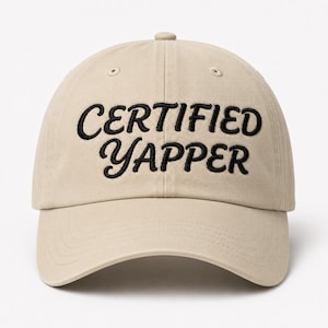 Puede incluir: Una gorra de béisbol de color beige con el texto CERTIFIED YAPPER bordado en hilo negro en la parte frontal. La gorra presenta una corona estructurada, una visera curva y ojales cosidos en los paneles superiores para la ventilación.