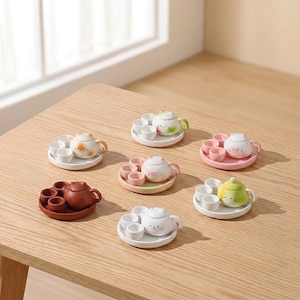 Puede incluir: Una colección de siete juegos de té de cerámica en miniatura, cada uno con una pequeña tetera con forma de gato, un plato a juego y tres tazas diminutas. Los juegos vienen en varios colores, incluyendo blanco, rosa, verde, marrón y patrones variados.