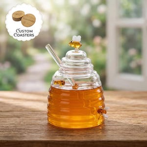 May include: A clear glass honey pot with a ribbed beehive shape, filled with golden honey. The lid features a small glass bee figurine, and two additional glass bees are attached to the sides. A clear glass honey dipper rests inside the pot.