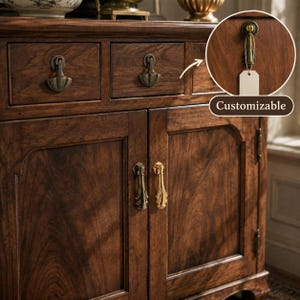 Puede incluir: Un mueble de madera marrón oscuro con dos cajones con tiradores de metal de estilo antiguo y dos puertas inferiores con tiradores verticales de metal. Un recuadro circular muestra un tirador con una etiqueta blanca y el texto Customizable.