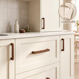 May include: A set of dark brown wooden cabinet handles installed on cream-colored kitchen cabinetry. The handles feature a smooth, elongated design with rounded edges. A circular inset shows a blank white tag with the text Customizable.