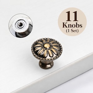 May include: A set of 11 bronze-toned metal cabinet knobs featuring a circular floral design with a beaded edge. The knobs have a central dome and a threaded metal insert on the back for mounting. The text 11 Knobs (1 Set) is visible.