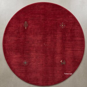 May include: A circular, red rug with embroidered gold-coloured geometric and nature-inspired designs. The rug features a tree, snowflake, and deer motif. The text "Fahad rugs" is visible on the bottom right.