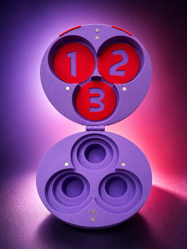 May include: A purple, hinged container with three circular compartments. The top section has three red circles with the numbers 1, 2, and 3. The bottom section has three empty circular spaces. The container is open, revealing the interior.