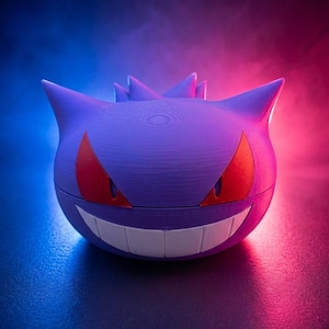 May include: A purple, spherical container with a smiling face, red eyes, and pointed ears. The container is designed to resemble a Gengar character. The background has a gradient of blue and pink.