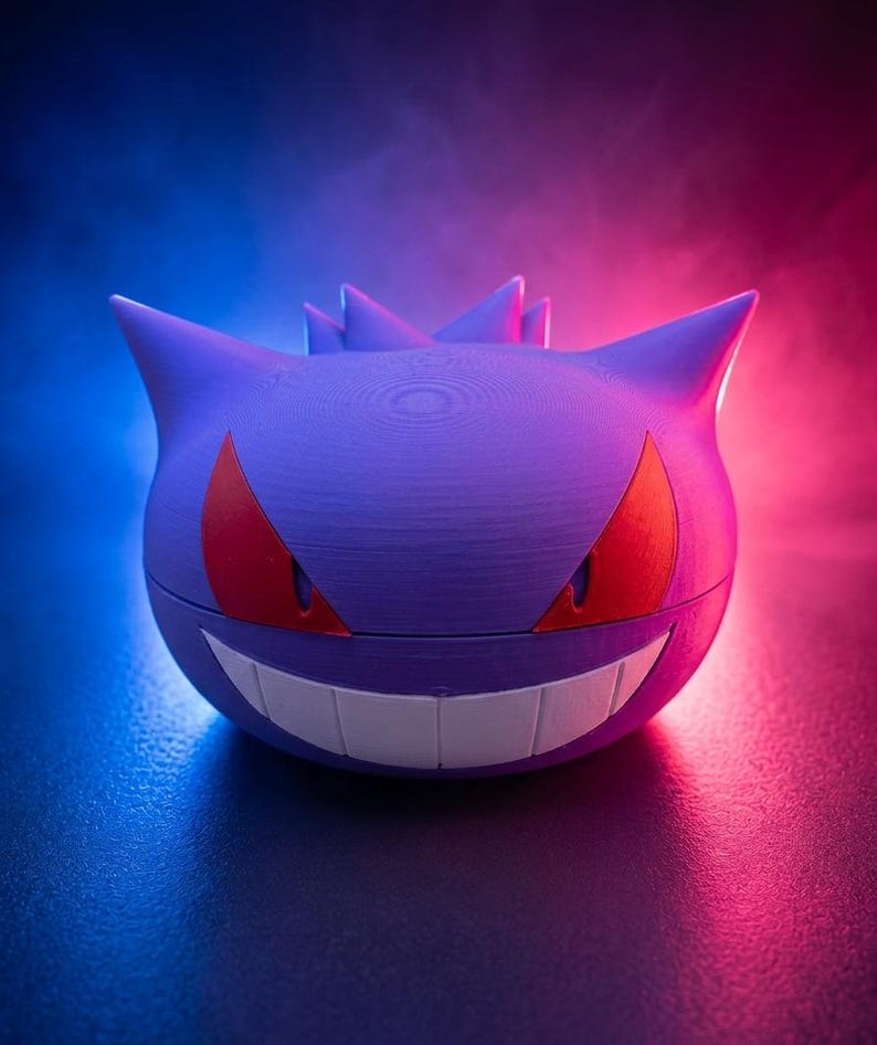 May include: A purple, spherical container with a smiling face, red eyes, and pointed ears. The container is designed to resemble a Gengar character. The background has a gradient of blue and pink.
