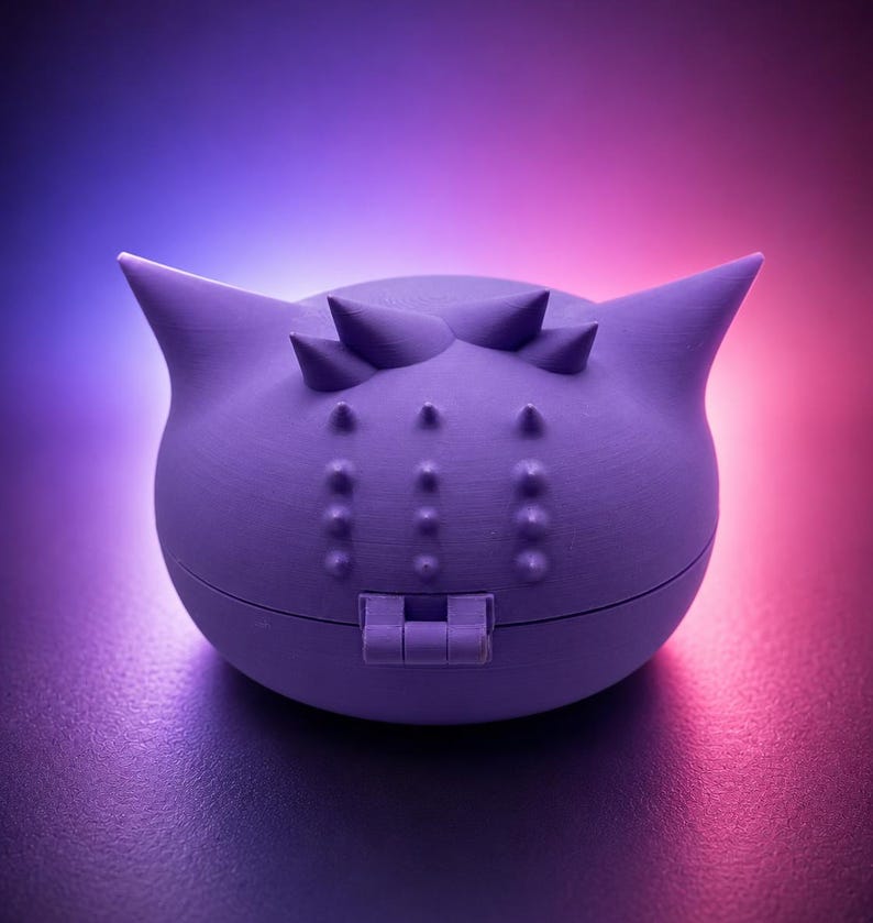May include: A lavender-colored, spherical container with a hinged closure. The container has a series of small, raised bumps and three pointed protrusions on top. The background transitions from blue to pink.