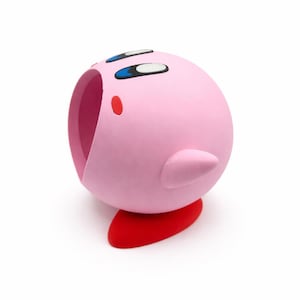 May include: A pink, spherical figurine with a red base, featuring large eyes and a small mouth. The figurine has a small, pointed ear-like protrusion on its side. The design is reminiscent of a popular video game character.