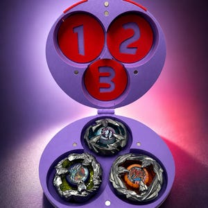 May include: A purple toy case with three red circles labeled 1, 2, and 3. The case is open, revealing three spinning tops with metallic silver and colorful designs. The background is a gradient of purple and red.