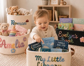 May include: Three off-white woven rope storage baskets and one black ribbed storage basket. The baskets feature embroidered names and phrases including Roman, Amelia, Evelyn's Book, and My Little Library, decorated with small crocheted flower accents.