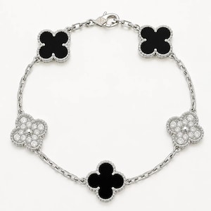 May include: A silver-toned bracelet featuring five clover-shaped motifs connected by a delicate chain. Three motifs are filled with smooth black onyx, while two motifs are encrusted with clear, sparkling round-cut stones. Includes a lobster clasp.