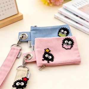 May include: Three small, colourful pouches with cartoon character patches. The pouches are light blue and pink, with silver zips and attached straps. The straps are pink and beige. The pouches have a fuzzy texture.