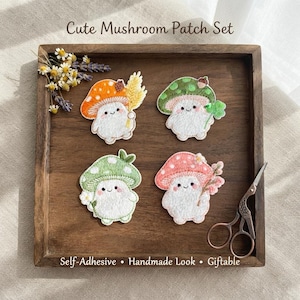 Puede incluir: Cuatro parches bordados que presentan hongos antropomórficos con cuerpos blancos y sombreros coloridos en naranja, verde y rosa. Los parches están dispuestos en una bandeja de madera con tijeras de estilo vintage y flores secas. Texto: Cute Mushroom Patch Set, Self-Adhesive, Handmade Look, Giftable.