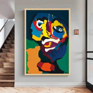 Puede incluir: Pintura de retrato abstracto con marco de madera. La obra presenta un rostro con colores llamativos, incluyendo azul, amarillo, rojo y verde. La pintura tiene un estilo de arte moderno y se exhibe en una pared gris.