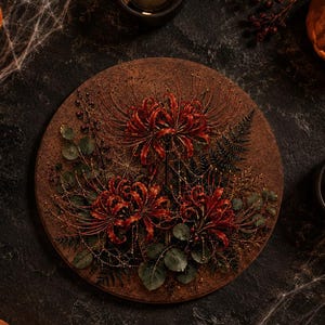 Könnte beinhalten: Eine kreisförmige Wandplatte mit einem gepressten Blumenarrangement aus dunkelroten Spinnenlilien, grünen Eukalyptusblättern und dunklen Farnen, umgeben von vier kleinen orangefarbenen Kürbissen und vier schwarzen Teelichtern auf dunklem Grund.