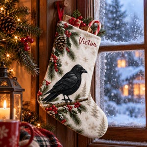 Puede incluir: Un calcetín navideño de color crema con un cuervo negro posado en una rama, rodeado de agujas de pino, piñas y bayas rojas. El nombre Victor está impreso en rojo cerca de la parte superior, con pequeñas cajas de regalo y un bastón de caramelo.