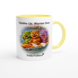 May include: White ceramic mug with a yellow interior and handle. The mug features a colorful illustration of three teddy bears in a boat with paddles, and the text "Paddles Up, Worries Down". The TeddyTrekkers logo is at the bottom.