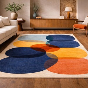 May include: A rectangular rug with an abstract design. The rug features overlapping oval shapes in shades of blue, orange, and yellow against a beige background. The rug is placed on a wooden floor.