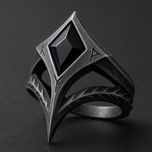 Op de afbeelding: Een zilverkleurige ring met een grote, zwarte, ruitvormige steen in het midden. De ring heeft een geometrisch ontwerp met gegraveerde symbolen en een puntige punt. De band heeft een bladerenpatroon. De ring staat tegen een donkere achtergrond.