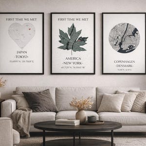 Op de afbeelding: Drie ingelijste prints met zwarte randen hangen boven een bank. De prints tonen kaartontwerpen in een hart, een esdoornblad en een cirkel. Tekst op de prints bevat "First Time We Met" en plaatsnamen zoals Tokio, New York en Kopenhagen.