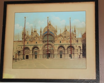 Puede incluir: Una impresión enmarcada de una pintura que representa la Basílica de San Marcos en Venecia, Italia. El edificio es una gran estructura adornada con una cúpula central y múltiples torres. La impresión está en un marco negro con un passe-partout blanco.