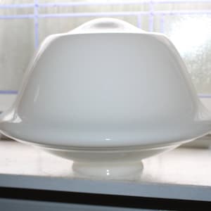 May include: A white glass lampshade with a rounded, bell-like shape. The lampshade has a smooth, glossy surface and a small, circular base. It is designed to diffuse light.