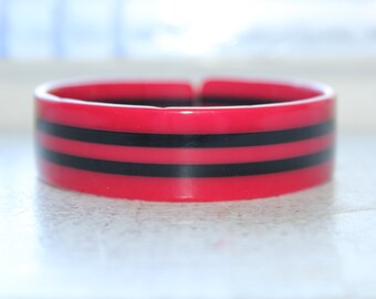 May include: A bright pink plastic bangle bracelet with two black stripes.