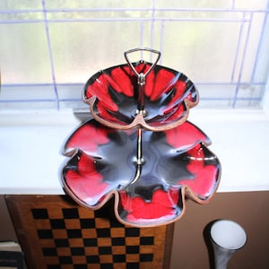 May include: Two-tiered serving tray with a black and red floral design. The tray is made of ceramic and has a metal stand.