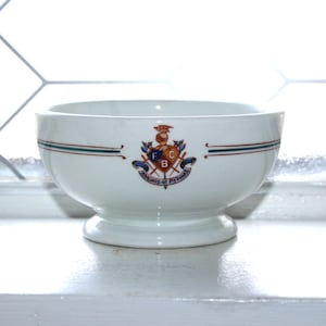 May include: White ceramic bowl with a pedestal base. The bowl features a crest with the text "Knights of Pythias" and red, green, and blue accents. A thin red and green stripe encircles the bowl near the rim.