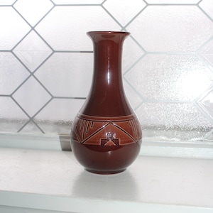 May include: A brown ceramic vase with a geometric design. The vase has a narrow neck and a rounded body.