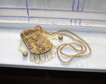 May include: A gold beaded drawstring bag with a fringe and a matching chain. The bag is decorated with gold embroidery.