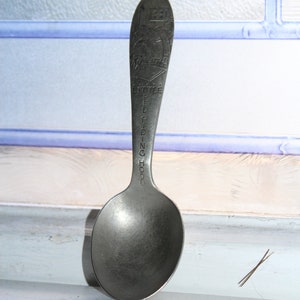 May include: A silver spoon with a rounded bowl and a long, slender handle. The handle is engraved with the words "Little Red Riding Hood".